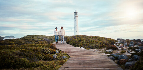 Romance, love and a couple holding hands while walking on the beach with a lighthouse in the background. Nature, view or blue sky mockup with a man and woman taking a romantic walk outside together