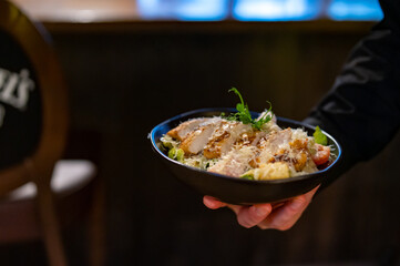 Men's waiter hands hold a Caesar salad with croutons, cheese, eggs, tomatoes and grilled chicken in...
