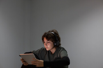 A teenage girl surfs the internet with a tablet or electronic device in a dimly lit room