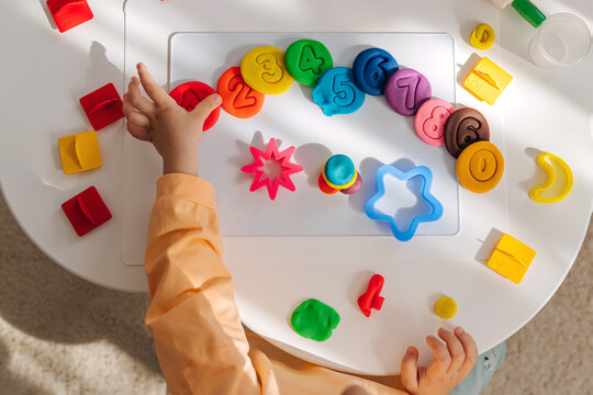 A little girl play with plasticine and creates colorful numbers.  Learning to count through play. Early education. Fine motor skills, creativity and  hobby.