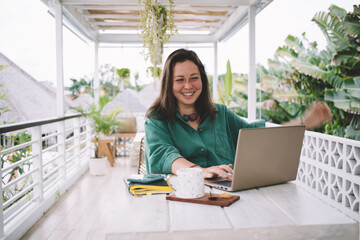 Happy Caucasian woman searching media application for installing on modern laptop computer, cheerful female blogger creating web content on portable netbook connecting to 4g wireless outdoors