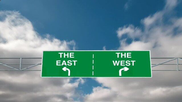 Zoom to an overhead road signs pointing the way in opposite directions to the east and to the west with timelapse white clouds in the background. The east west divide. 