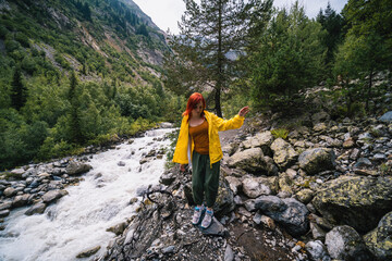 Woman in yellow jacket, tourist hiking track to the Chalaadi glacier. in the background turbulent flow of the river, Georgia, Mestia. Travel and vacation concept.