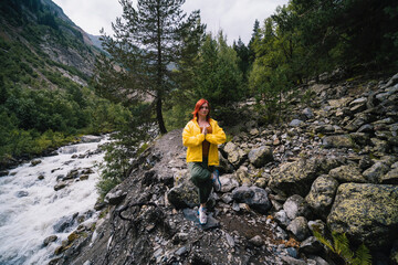 Woman in yellow jacket, tourist hiking track to the Chalaadi glacier. turbulent flow of the river, Yoga pose, meditation Georgia, Mestia. Travel and vacation concept.