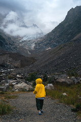 Traveling along mountains, freedom and active lifestyle, destination concept. Woman tourist in yellow jacket standing on mountain in Svaneti, Georgia near Chalaadi glacier hiking trail. Vertical photo