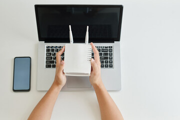 Hands of freelancer setting wi-fi router to work on laptop, view from above