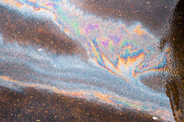 Oil slick on the asphalt road background. Rainbow gasoline oil spill on the pavement as a texture or background.