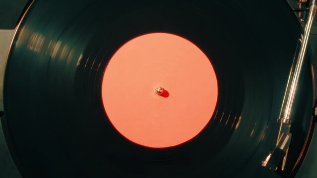 Close-up of a vinyl record with a orange sticker spinning on a retro turntable from top view. Black retro vinyl record on an old player. Close-up of a rotating plate on a player