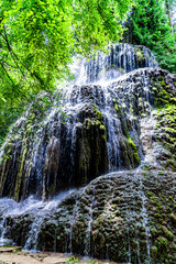 large multiple waterfall of colorful water in a river, with many stones and a multitude of trees.