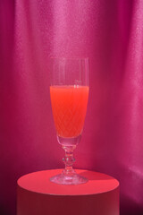 A glass of red champagne wine in a crystal on a red stand. Magenta curtains background.