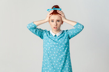 Astonished scared red haired woman standing with hands on her head, sees something shocked.