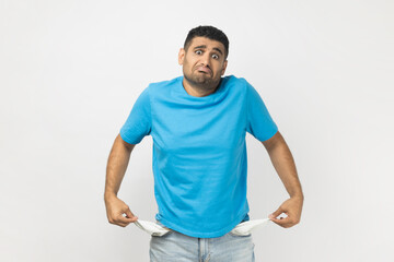 Sad poor attractive man in T- shirt standing showing his empty pockets, has no money, lost his job.