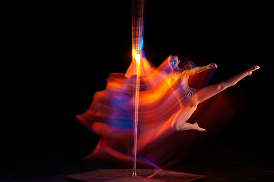 Spinning around. Young girl performing pole dance isolated over black studio background with mixed neon lights. Concept of sport and dance, beauty of movements, action, modern style