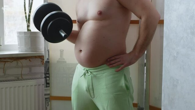 A fat person with a hand dumbbell. People suffering from obesity, a person with a thick belly shakes the biceps. The concept of losing weight in the gym.