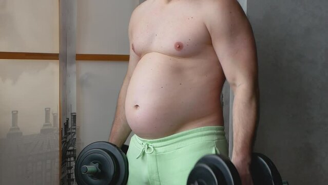 A fat person with a hand dumbbell. People with obesity, a person with a thick belly shakes the biceps. The concept of losing weight in the gym.