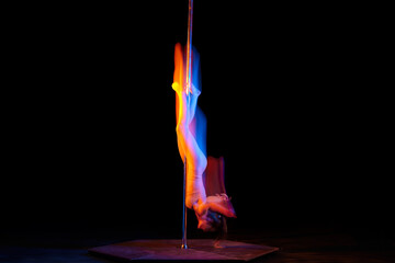 Upside down. Line. Young girl performing pole dance isolated over black studio background with...