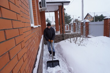 A man cleans snow in the winter in the courtyard of the house.