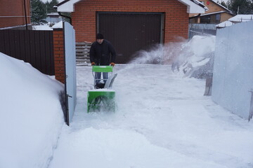 A man cleans snow in the winter in the courtyard of the house,  man cleaning snow with a snow blower