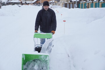 A man cleans snow in the winter in the courtyard of the house,  man cleaning snow with a snow blower