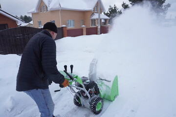 A man cleans snow in the winter in the courtyard of the house,  man cleaning snow with a snow blower