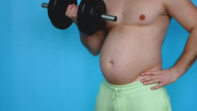A fat man does an exercise with dumbbells for two hands on a blue studio background, a fat man with a big belly. A fat man shakes his biceps. Obesity people