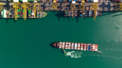 commercial port loading and unloading cargo from container ship import and export by crane for distributing goods by trailers transported to customers and dealers, aerial top view.