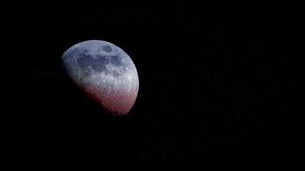 Close-up color photo of the moon shaded with red, white and blue colors against a black background. Copy space.