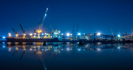 shipyard dry dock maintenance and repair container ship transport and oil ship tanker, crane work and commercial port reflection in water, at night over lighting in sea long exposure blue color tone, - obrazy, fototapety, plakaty