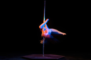 Passionate hobby. Young artistic girl performing pole dance isolated over black studio background with mixed neon lights. Concept of sport and dance, beauty of movements, action, modern style