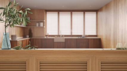 Fototapeta na wymiar Wooden table top, cabinet, panel or shelf with shutters close up. Olive branch in vase and candles. Blurred background with white modern japandi kitchen, interior design