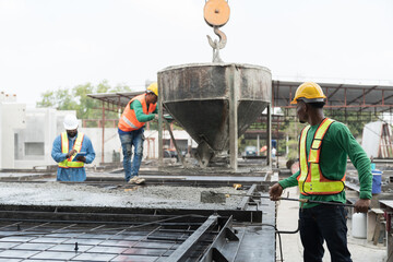 Construction workers pouring wet concrete by concrete bucket for building precast concrete wall at...