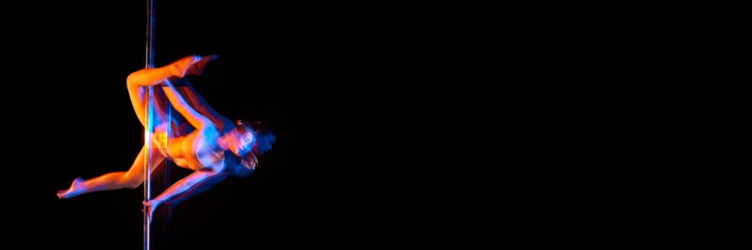 Strength. Young girl performing pole dance isolated on black studio background with mixed neon lights. Concept of sport and dance, beauty of movements, action, modern style. Banner. Copy space for ad
