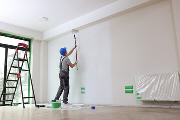 Male painter paints house wall with roller brush. - obrazy, fototapety, plakaty