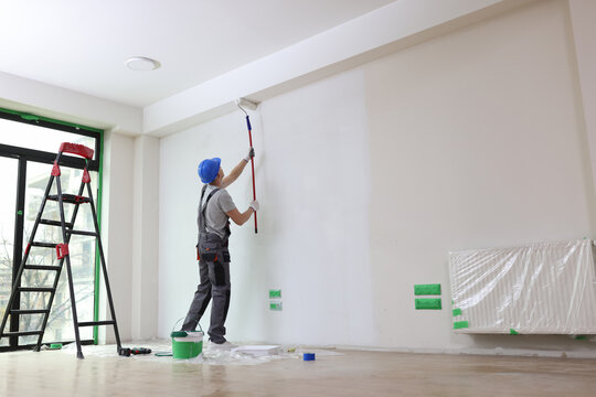 Male painter paints house wall with roller brush.