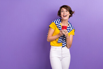 Photo of shiny dreamy woman wear tied sweater looking empty space texting modern gadget isolated purple color background