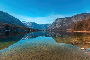 Beautiful scenic landscape of glacial Bohinj lake in Slovenia with crystal clear water and rocky shore on sunny winter morning