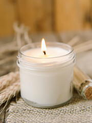 Handmade candle in a glass on burlap and wooden background. Scented candle and ears of wheat. Natural. Soft focus