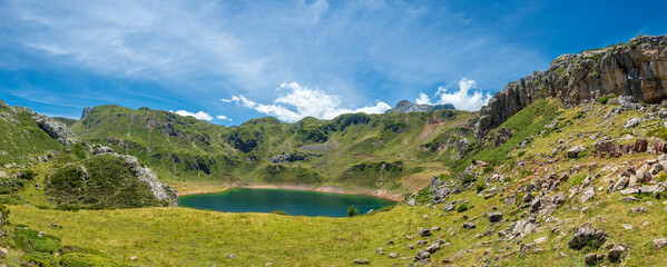 Fototapeta na wymiar panorámica de un lago de alta montaña rodeado de hierba y de montañas con el cielo azul