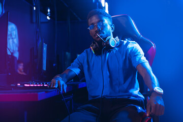 Portrait young American African man professional gamer of online video game with headphones, neon background in computer club - obrazy, fototapety, plakaty