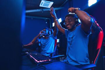 African Streamers young mans rejoices in victory professional gamer playing online games computer with headphones, neon color - obrazy, fototapety, plakaty