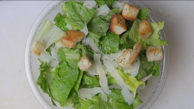 Slow motion footage of croutons being put on a caesar salad shot from directly above