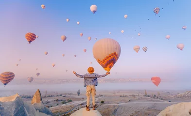 Poster Traveler man in hat background landscape Cappadocia with hot air balloons sun light. Concept trip Turkey travel © Parilov