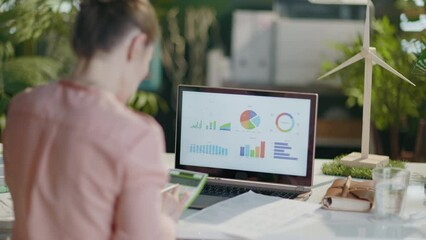 Seen from behind modern business woman with calculator and laptop exploring graphs in modern office. - Powered by Adobe