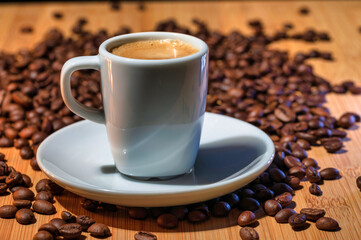A cup of rich espresso on a saucer with a spoon, surrounded by roasted coffee beans on a wooden table, perfect for a coffee shop promotion. 