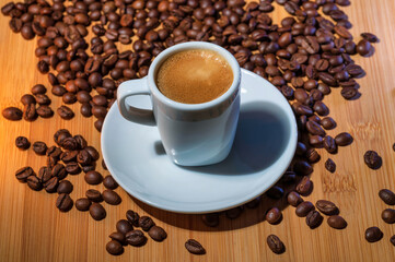 A cup of rich espresso on a saucer with a spoon, surrounded by roasted coffee beans on a wooden table, perfect for a coffee shop promotion. 