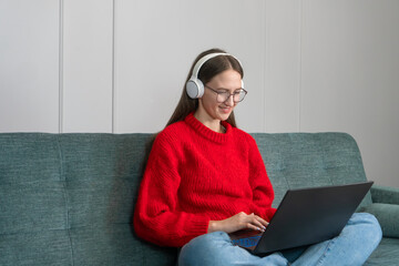 Young woman wearing headphones holds conference calls on a laptop, talks to an online teacher, studies, works from home. Student studying online using a computer chat via webcam. Distance education