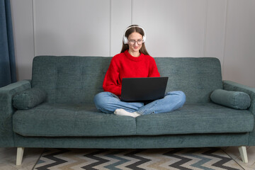 Young woman wearing headphones holds conference calls on a laptop, talks to an online teacher, studies, works from home. Student studying online using a computer chat via webcam. Distance education