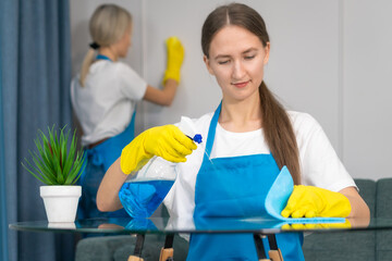 Close up staff of the cleaning service with professional equipment is engaged in cleaning the house, hygiene. Young woman in uniform wipes the table with a cleaning agent, microfiber cloths.