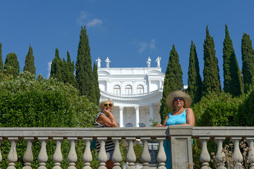 Women are posing near balustrade in park with white building.