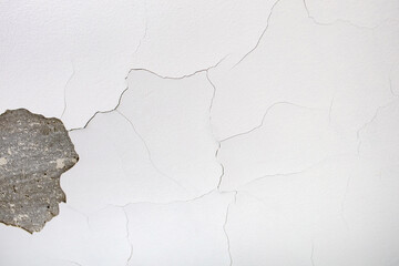 A white wall in cracks with fallen plaster and in need of repair. Wall background with cracks. Free...